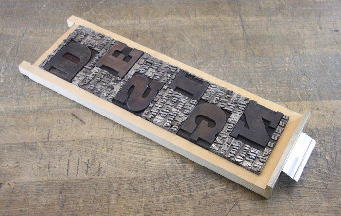 Drukblokken - een letterbak gevuld met een collage “DESIGN”, Antiek en Kunst, Antiek | Wandborden en Tegels