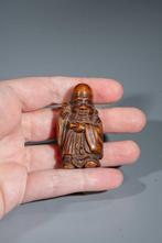 Een Japanse houten netsuke die een staande wijze afbeeldt,